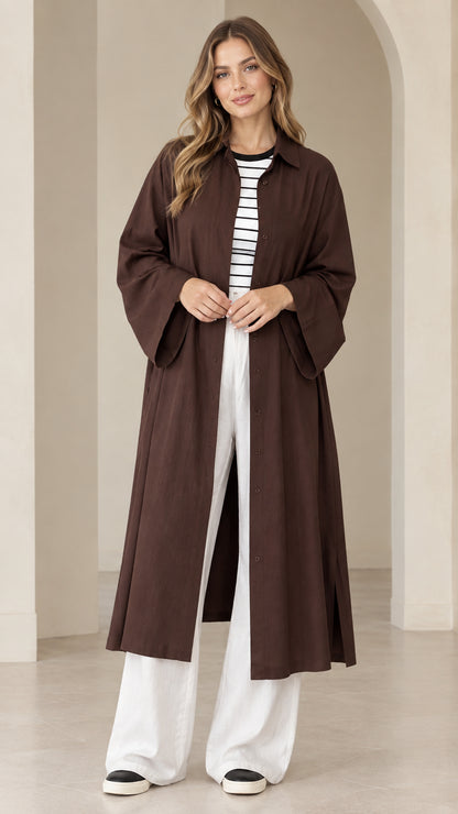 Front view of model wearing dark brown longline duster shirt dress with white wide-leg trousers