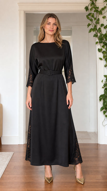 Front view of model wearing black satin boatneck maxi dress with lace trim and belt