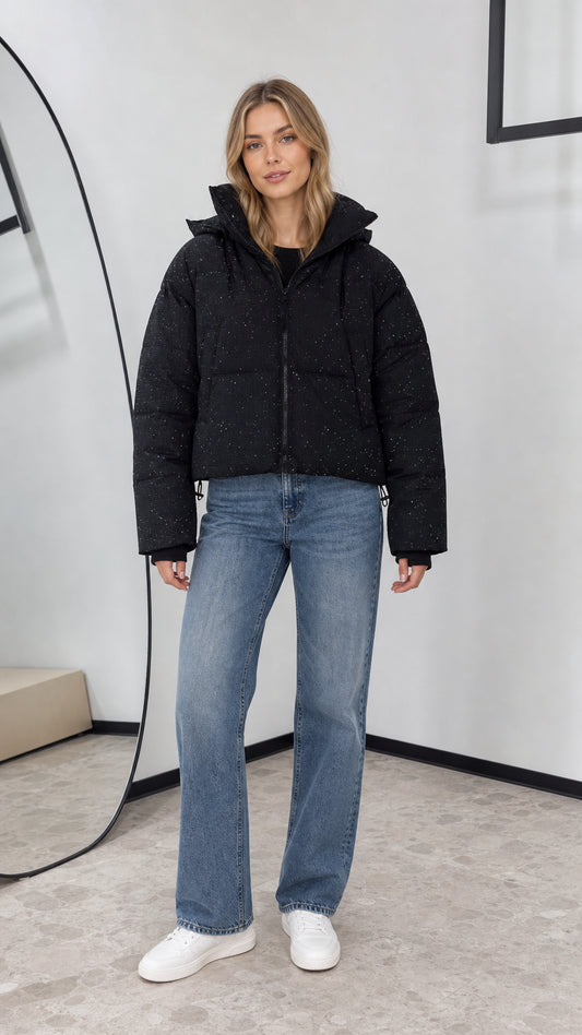 Front view of woman wearing black shimmer cropped hooded puffer jacket with wide-leg jeans