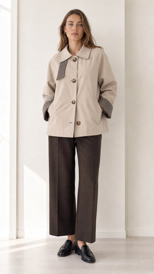 Front view of women's beige short trench jacket with houndstooth trim and dark trousers