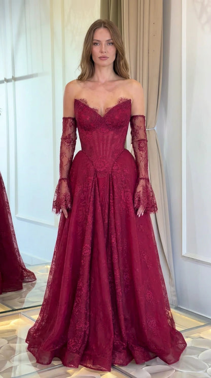 Front view of model wearing burgundy strapless floral lace corset evening gown with matching lace sleeves