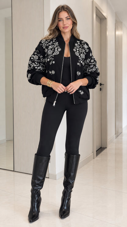 Full front view of model wearing black floral embroidered bomber jacket with black pants and boots