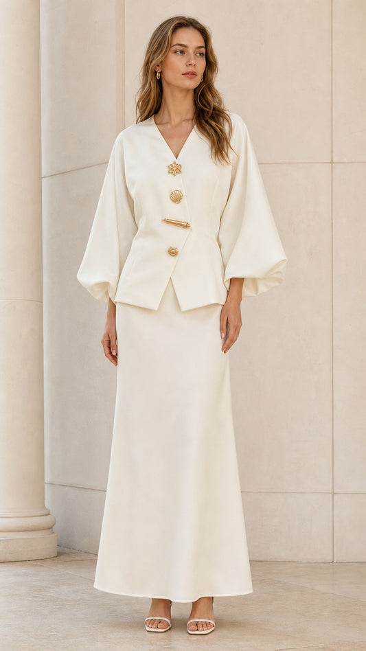 Full front view of model wearing ivory V-neck top with lantern sleeves and matching maxi skirt set with gold buttons