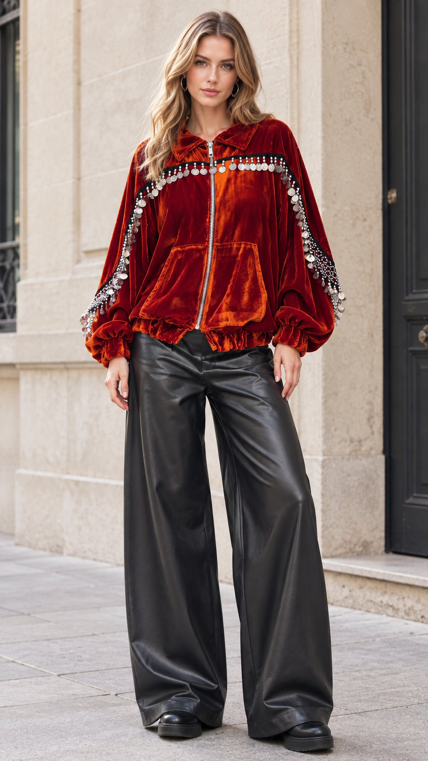 Front view of model wearing rust velvet zip-up jacket with coin fringe trims and black wide-leg trousers