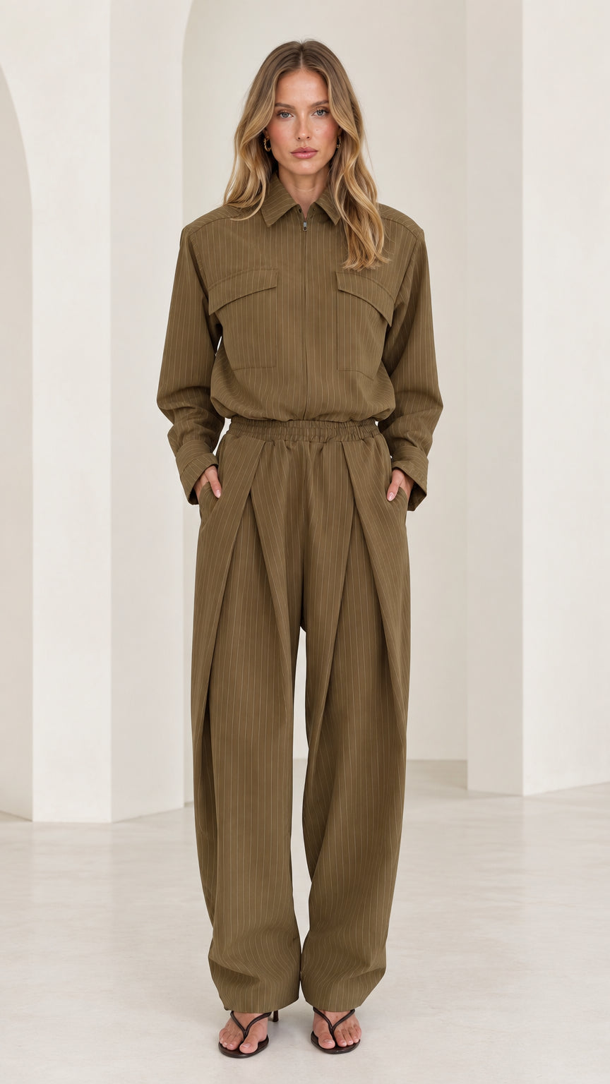 Front full-length view of woman wearing olive green long sleeve pleated wide-leg utility jumpsuit