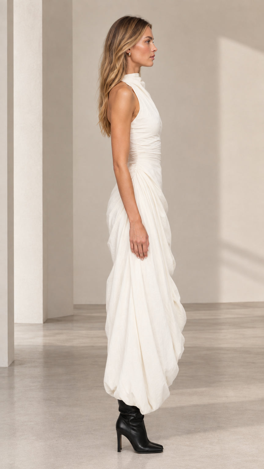 Side profile of model in ivory sleeveless draped maxi dress with bubble hem