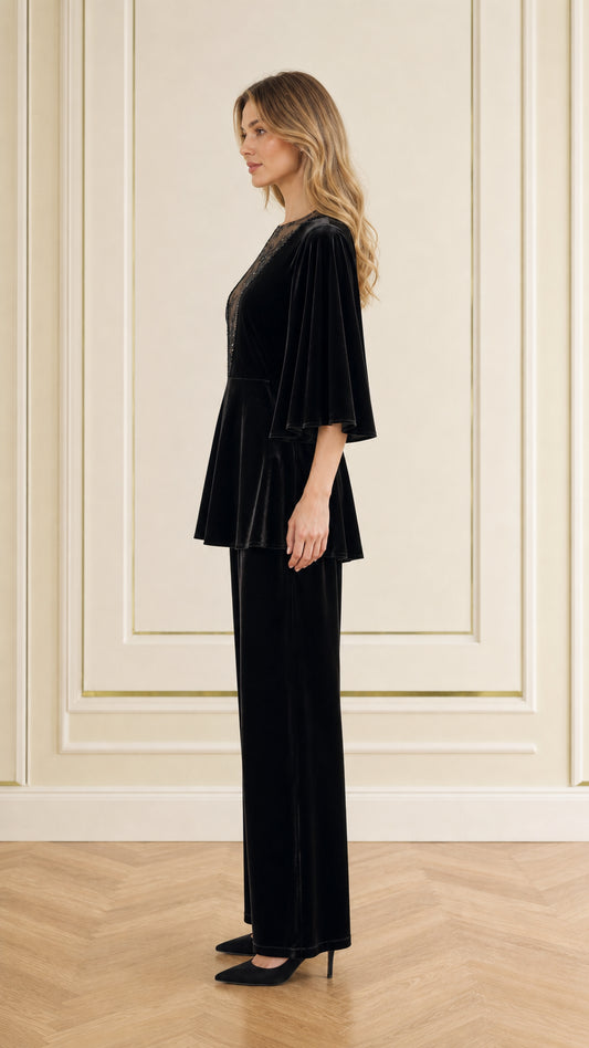 Side profile view of woman modeling black velvet peplum top and wide-leg trousers