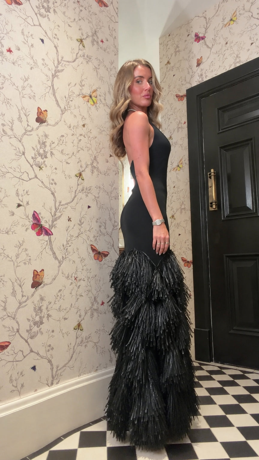 Side profile view of woman wearing black halter fringe mermaid gown