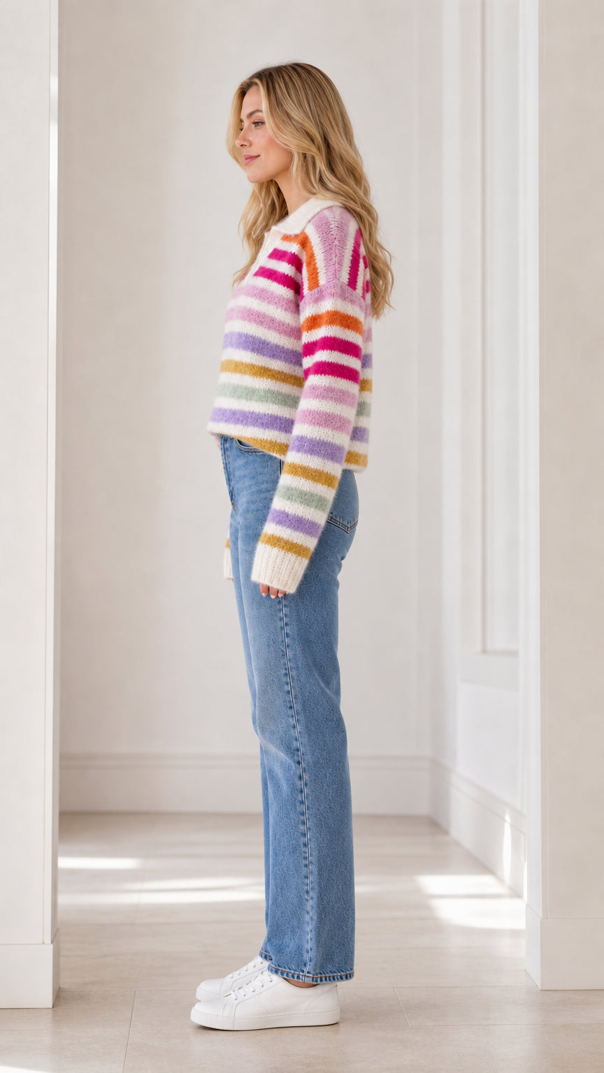 Side full view of woman wearing cream multicolor striped polo sweater with jeans and white sneakers