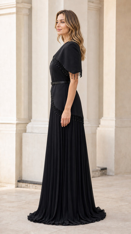 Side profile view of woman wearing black capelet maxi dress with pleated skirt