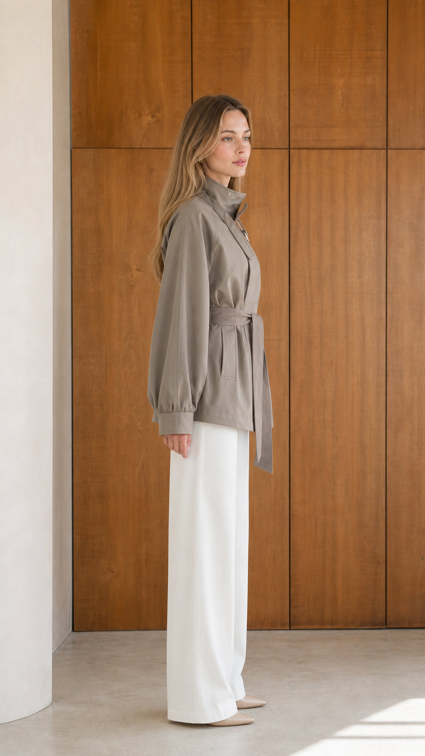 Side profile of model wearing taupe high neck short trench jacket with waist tie