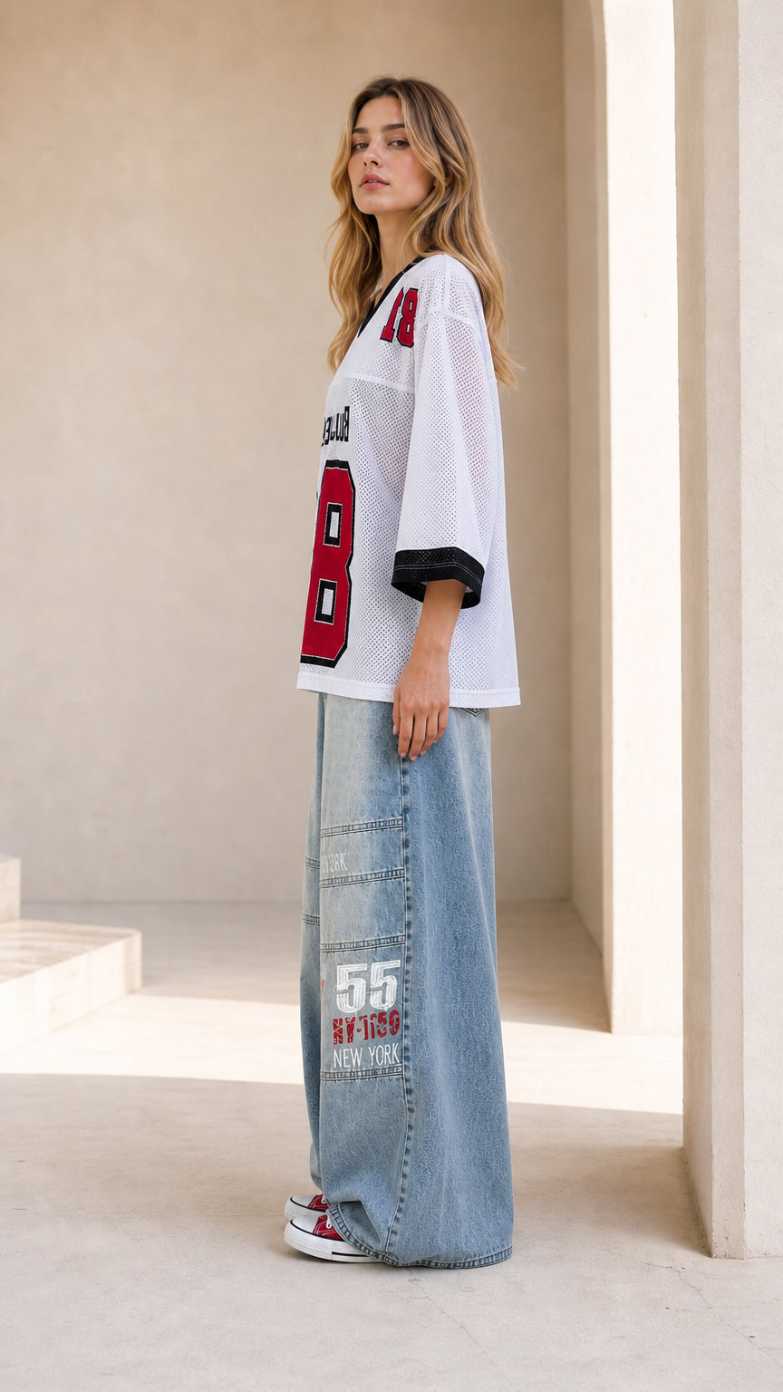 Side profile view of woman modeling white athletic mesh V-neck top and wide-leg denim