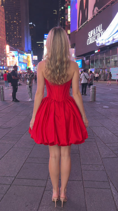 Back view of model in red strapless mini dress showing fitted back and bubble hem
