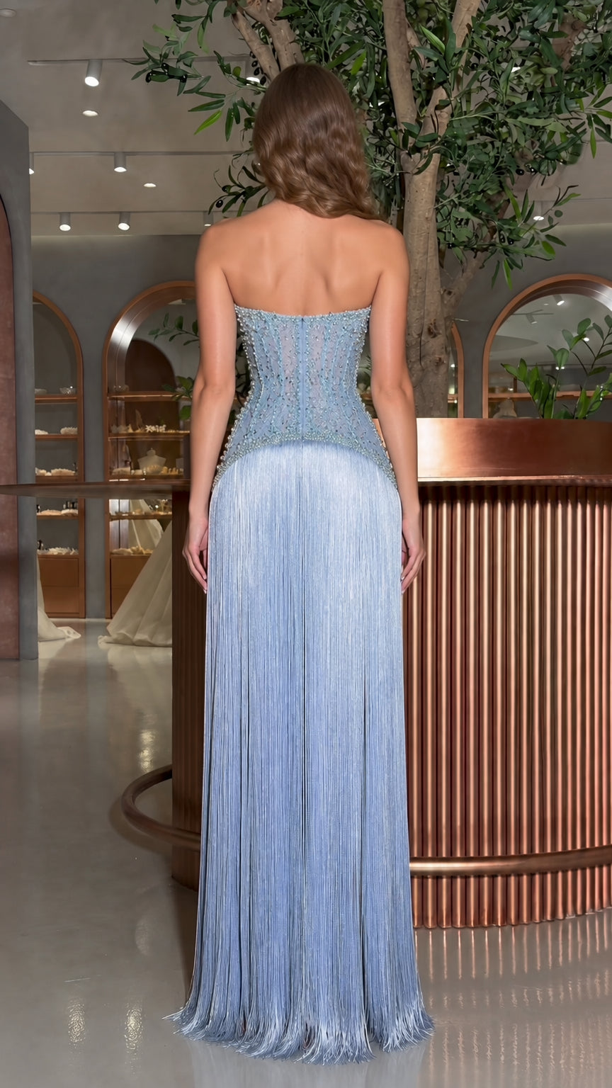 Back view of model in the light blue strapless corset maxi dress with flowing fringe
