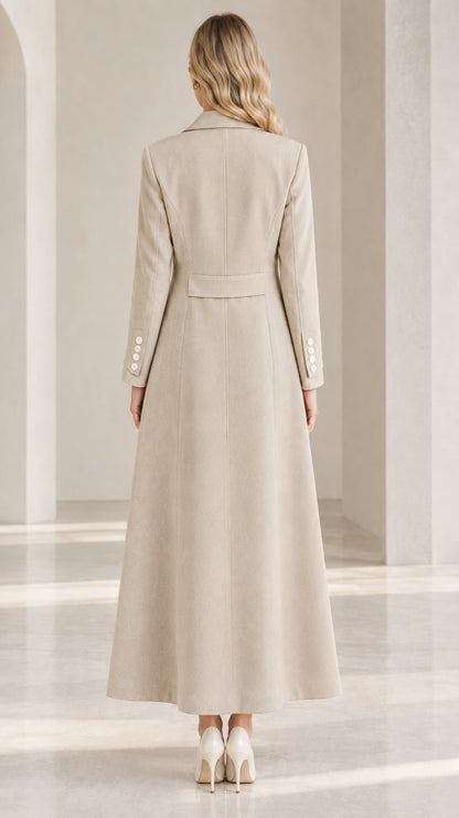 Back view of woman wearing the beige maxi coat highlighting the structured back waist tab and sweeping hem