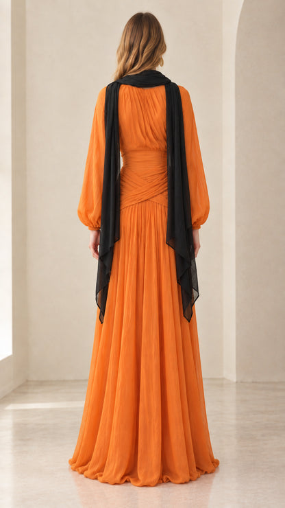 Back view of orange pleated dress showing flowing black cape scarf detail