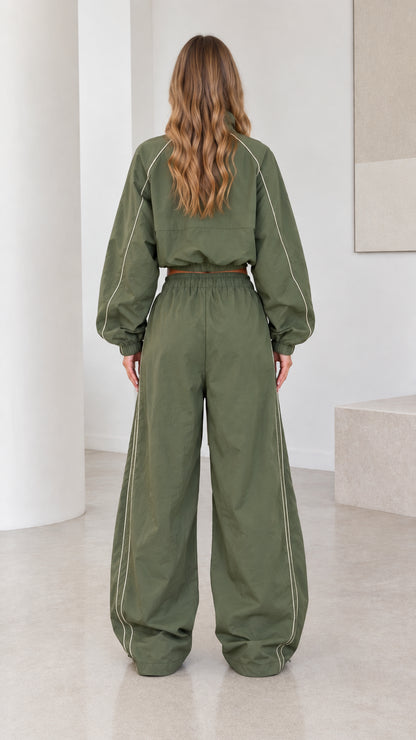 Back view of model wearing olive green cropped jacket and loose parachute pants