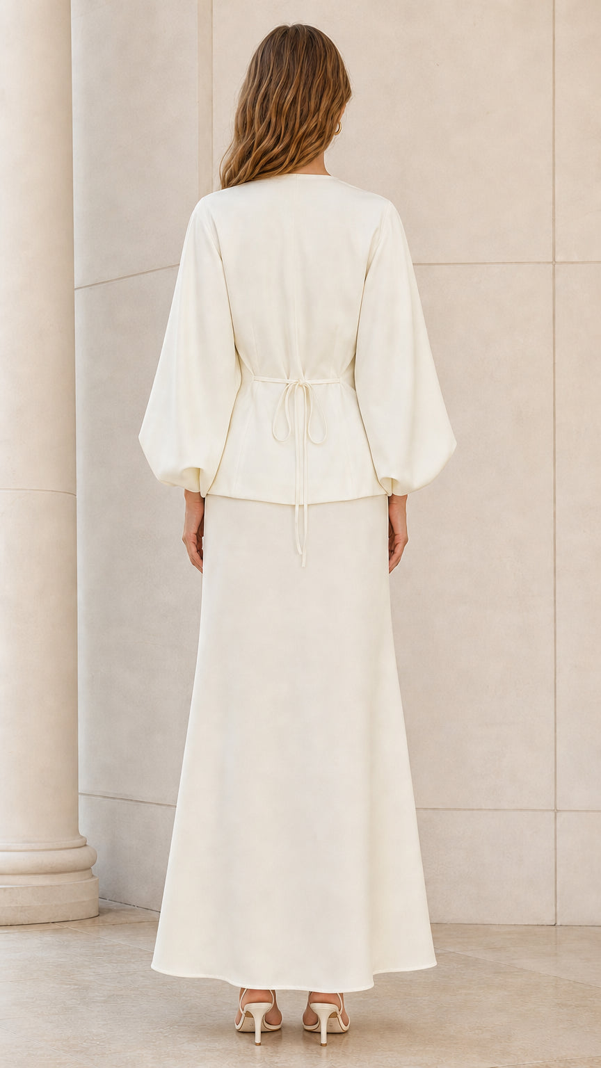 Back view of model wearing ivory lantern sleeve top with back waist tie and matching maxi skirt