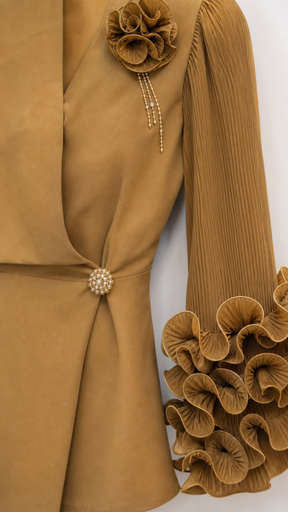 Close-up detail of 3D fabric flower corsage, jeweled button, and pleated ruffle sleeve in camel