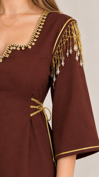 Close-up detail of gold beaded neckline trim, dangling shoulder tassels, and waist cords on brown dress