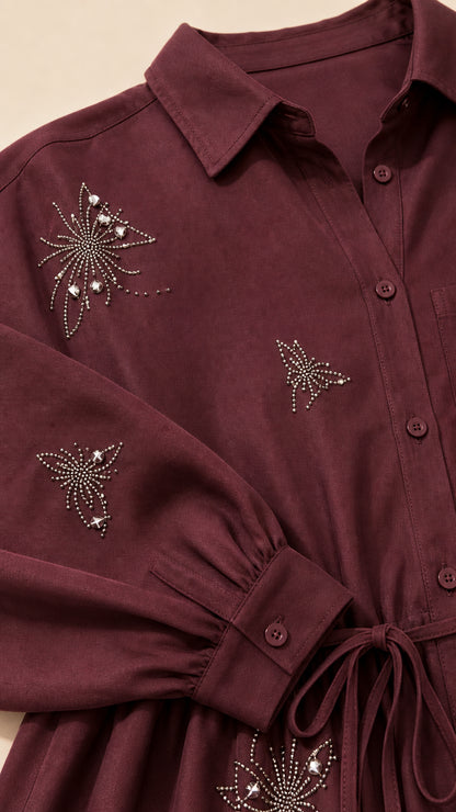 Close-up detail of rhinestone butterfly and starburst embellishments on burgundy collared top