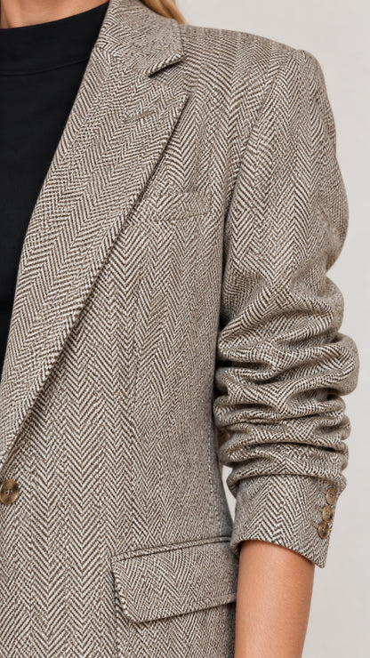 Close-up detail of herringbone textured fabric, notched lapel, and flap pocket