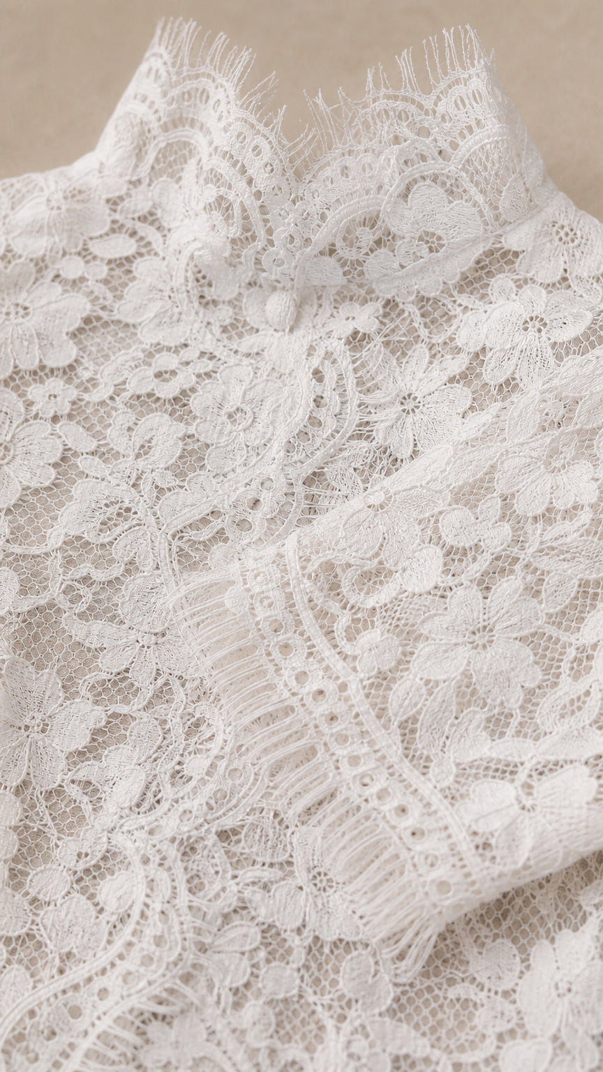 Detailed close-up of white floral eyelash lace fabric and scalloped mock collar