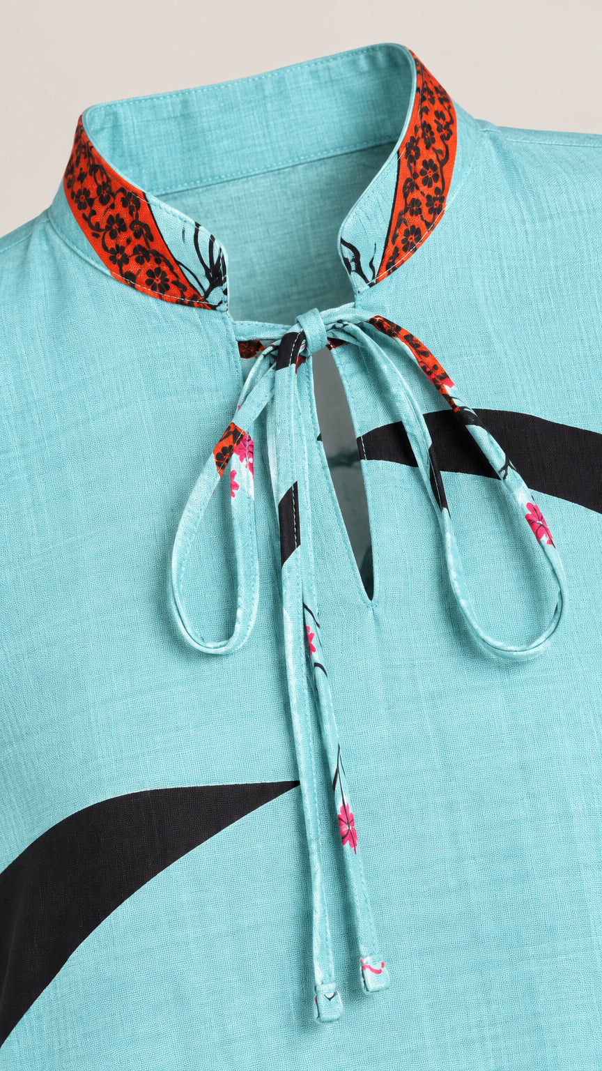 Close-up detail of sky blue textured fabric, tie-neck collar, and printed accents