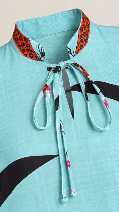Close-up detail of sky blue textured fabric, tie-neck collar, and printed accents