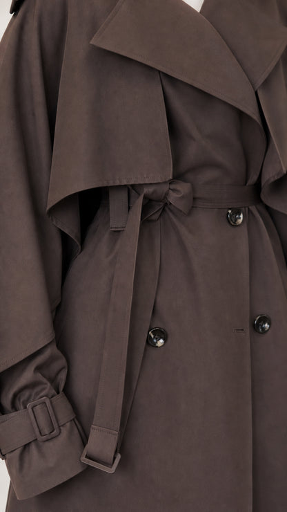 Close-up of dark brown trench coat cape overlay, belt buckle, cuff strap, and buttons