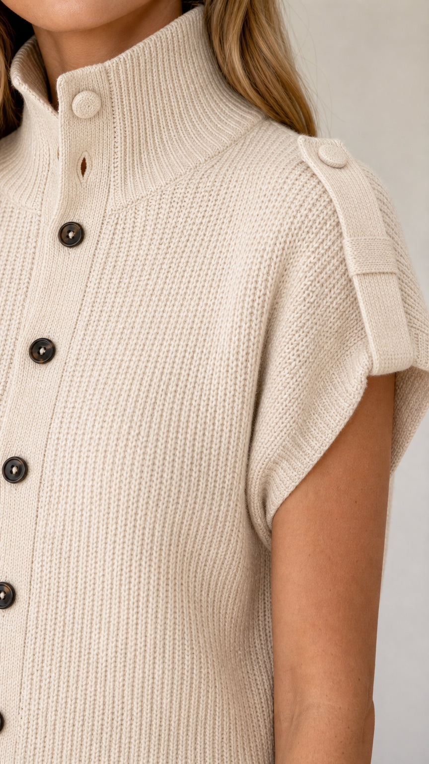 Close-up detail of beige ribbed knit texture, stand collar, buttons, and shoulder tab