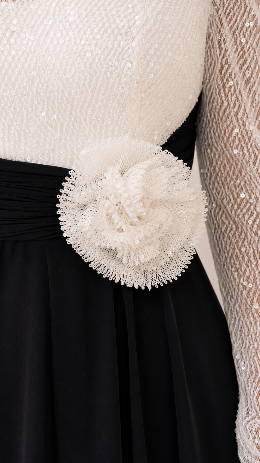 Close-up detail of white sequin bodice, pleated waistband, and textured 3D floral appliqué