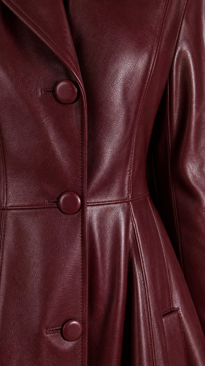 Close-up detail of covered buttons and grained faux leather texture on burgundy coat dress