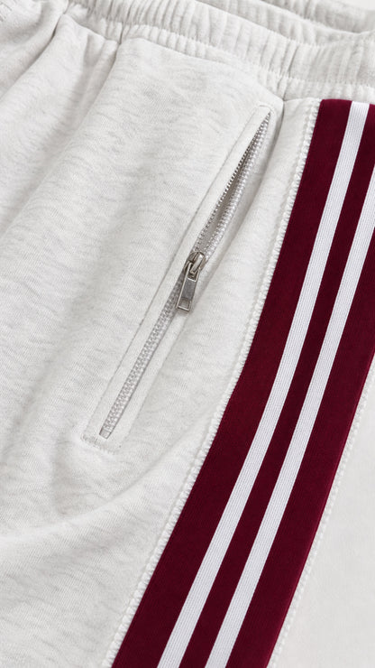 Close-up detail of white track pant zipper pocket and striped side trim