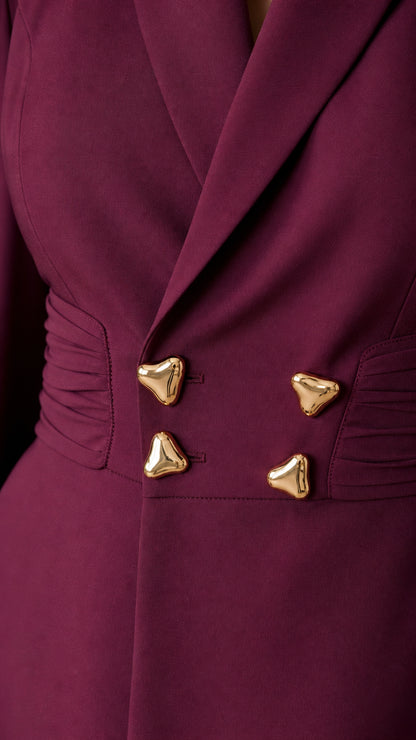 Close-up of ruched side waist detail with sculptural gold buttons on burgundy blazer