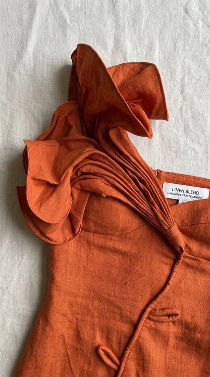Close-up of rust linen fabric with sculptural ruffle and woven tag