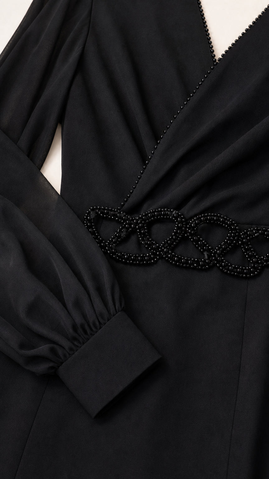 Close-up detail of beaded trim on surplice neckline and beaded waist appliqué on black dress