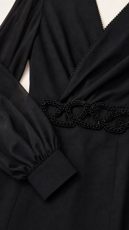 Close-up detail of beaded trim on surplice neckline and beaded waist appliqué on black dress