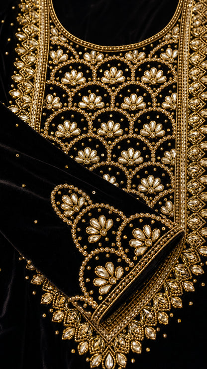 Close-up detail of ornate gold metallic embroidery and beadwork on black velvet neckline and cuff