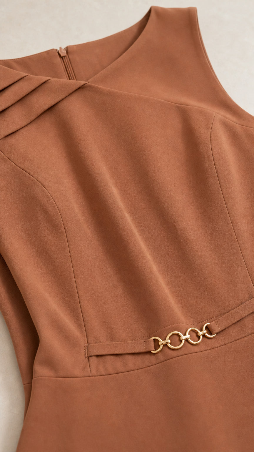 Close-up of asymmetrical pleated neckline and gold-tone waist chain accent on caramel brown dress