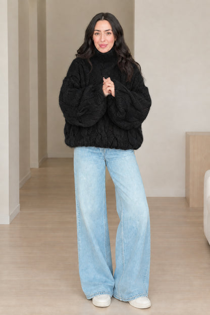 Front view of model wearing black chunky cable knit turtleneck sweater with wide-leg jeans