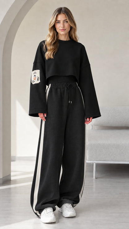 Model wearing black 2-piece cropped sweatshirt and wide leg track pants set with white side stripe
