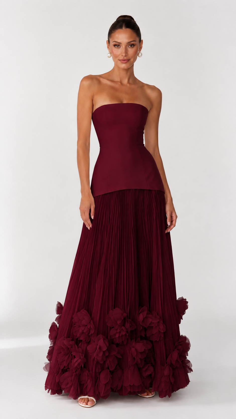Front view of burgundy strapless maxi gown with pleated skirt and floral hem