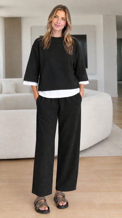 Full-body studio view of woman in black two-piece lounge set with white contrast trim